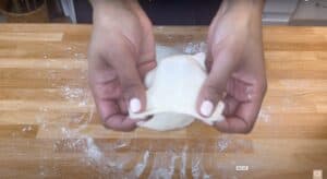 Hands stretching pizza dough on a floured wooden surface.